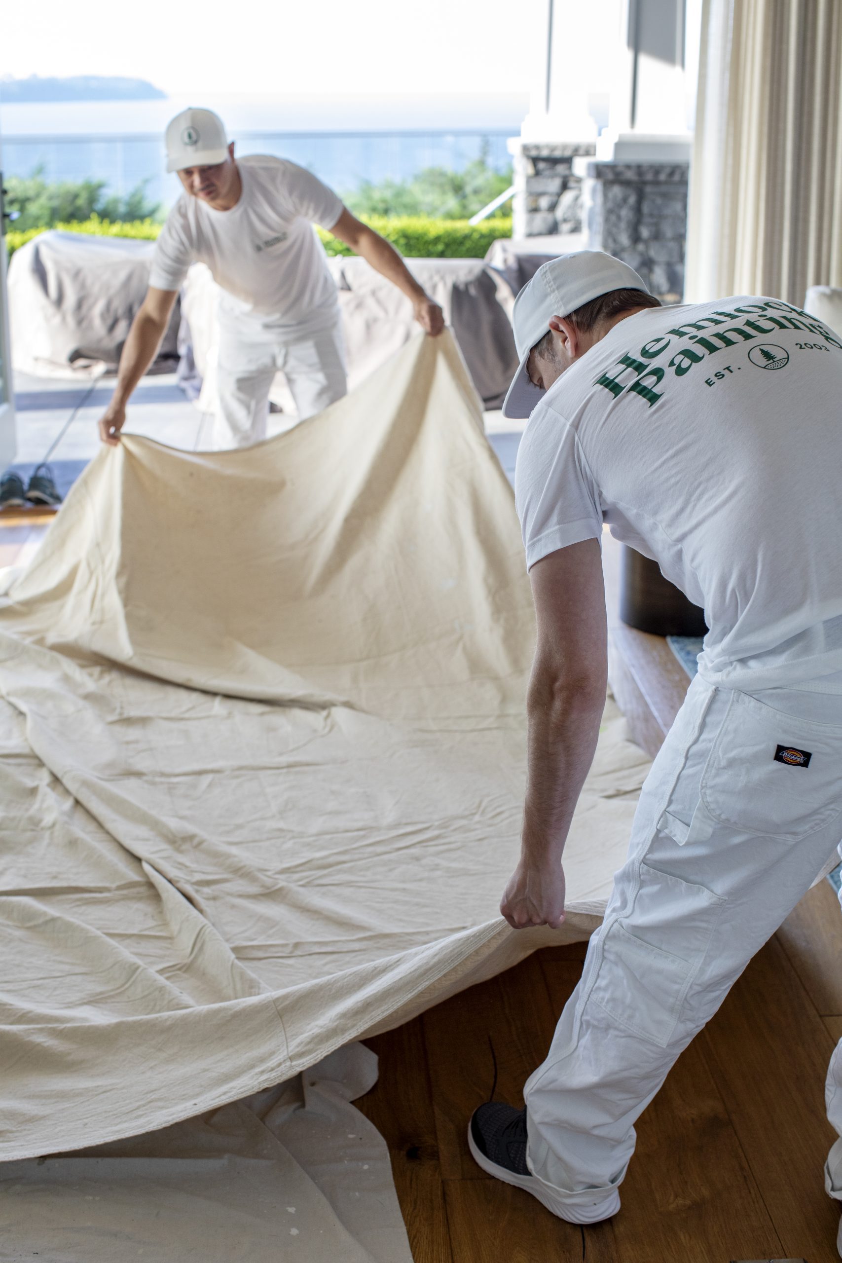 Hemlock Painting painters prepare for interior house painting by unraveling a sheet to protect the floor.